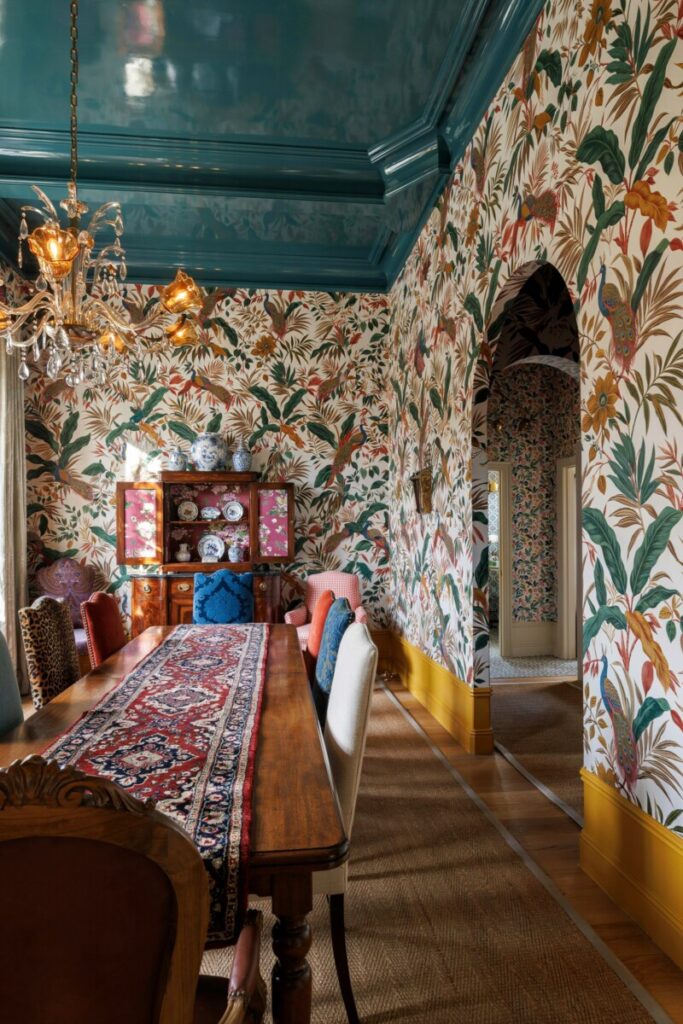 A dining room with a lacquered teal ceiling, patterned wallpaper on the walls
