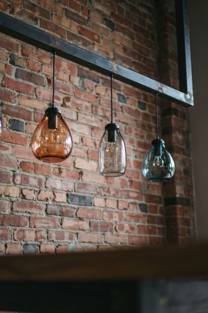 Colored glass industrial pendant lights hanging in front of a dark exposed brick wall7