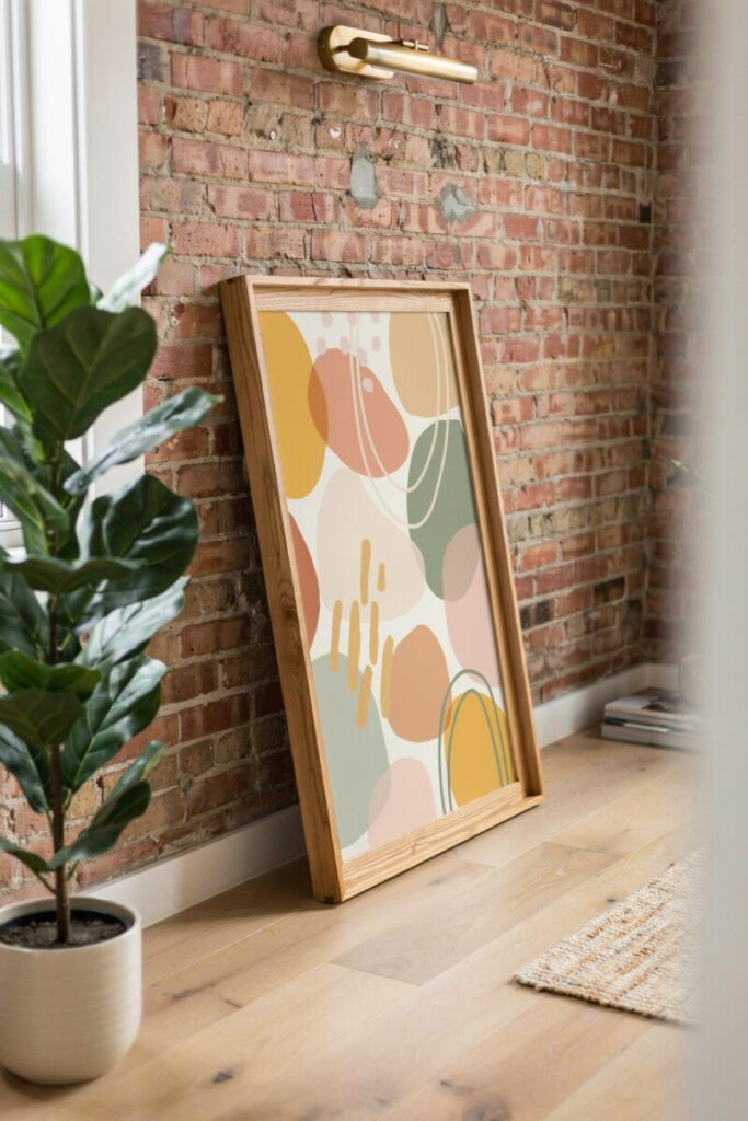 DIY renter-friendly framed peel-and-stick wallpaper panel leaning against an exposed brick wall next to a potted plant